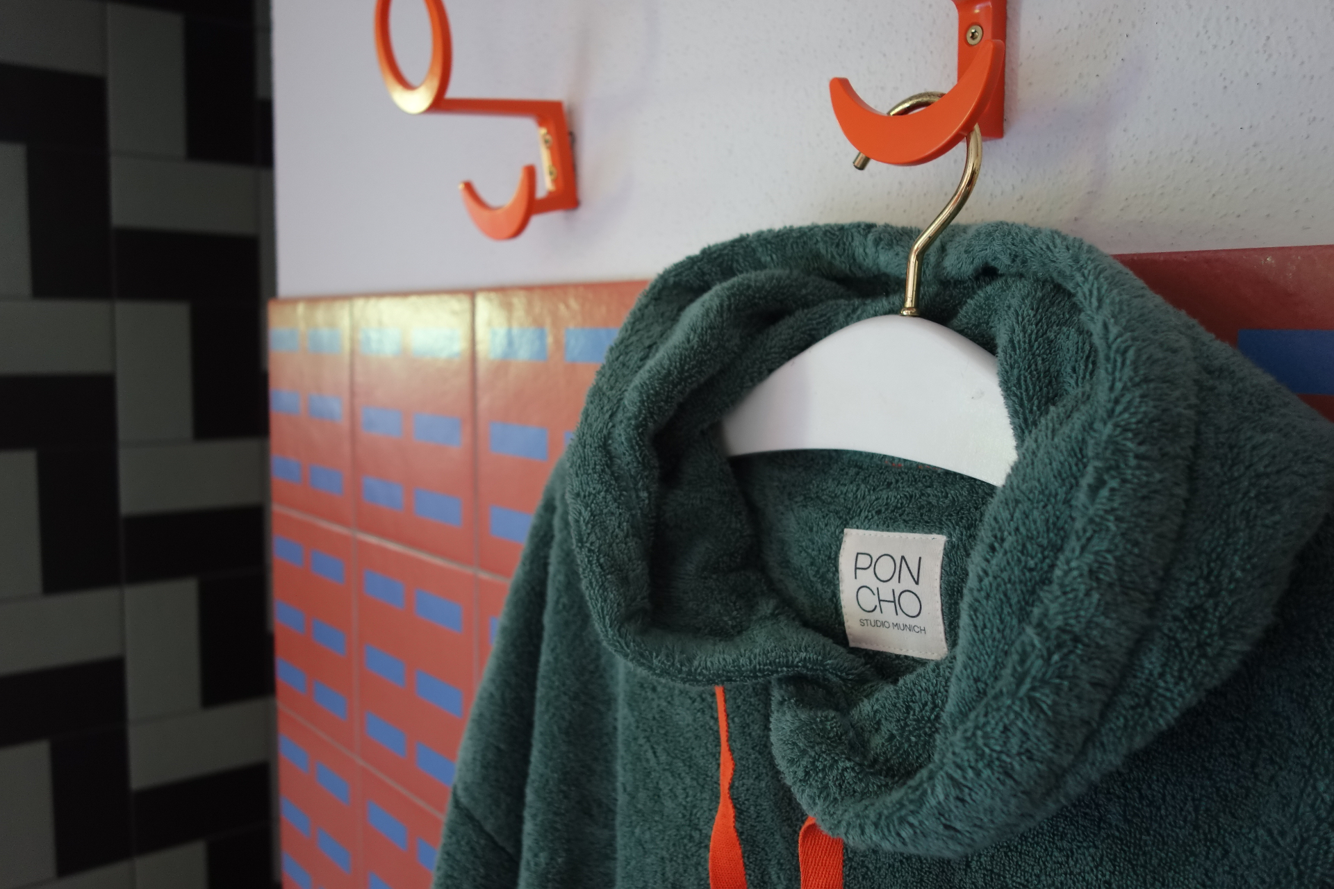 Teal terry cloth poncho hanging on a brass hanger